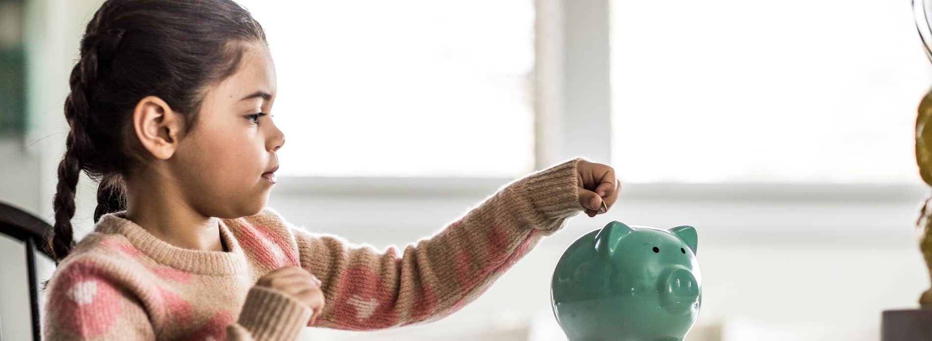 Young girl putting money in a piggy bank