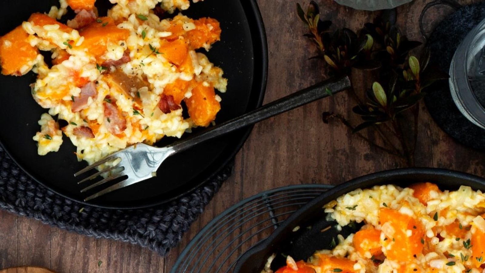 Butternut squash bacon risotto in black dish on a rustic table with fresh thyme