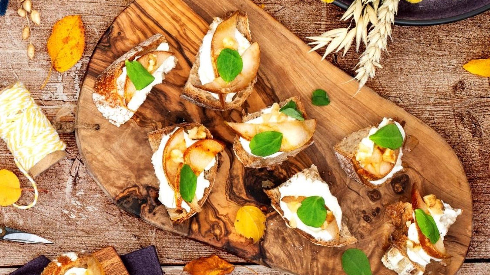 Pear goats cheese crostini on wooden board with basil