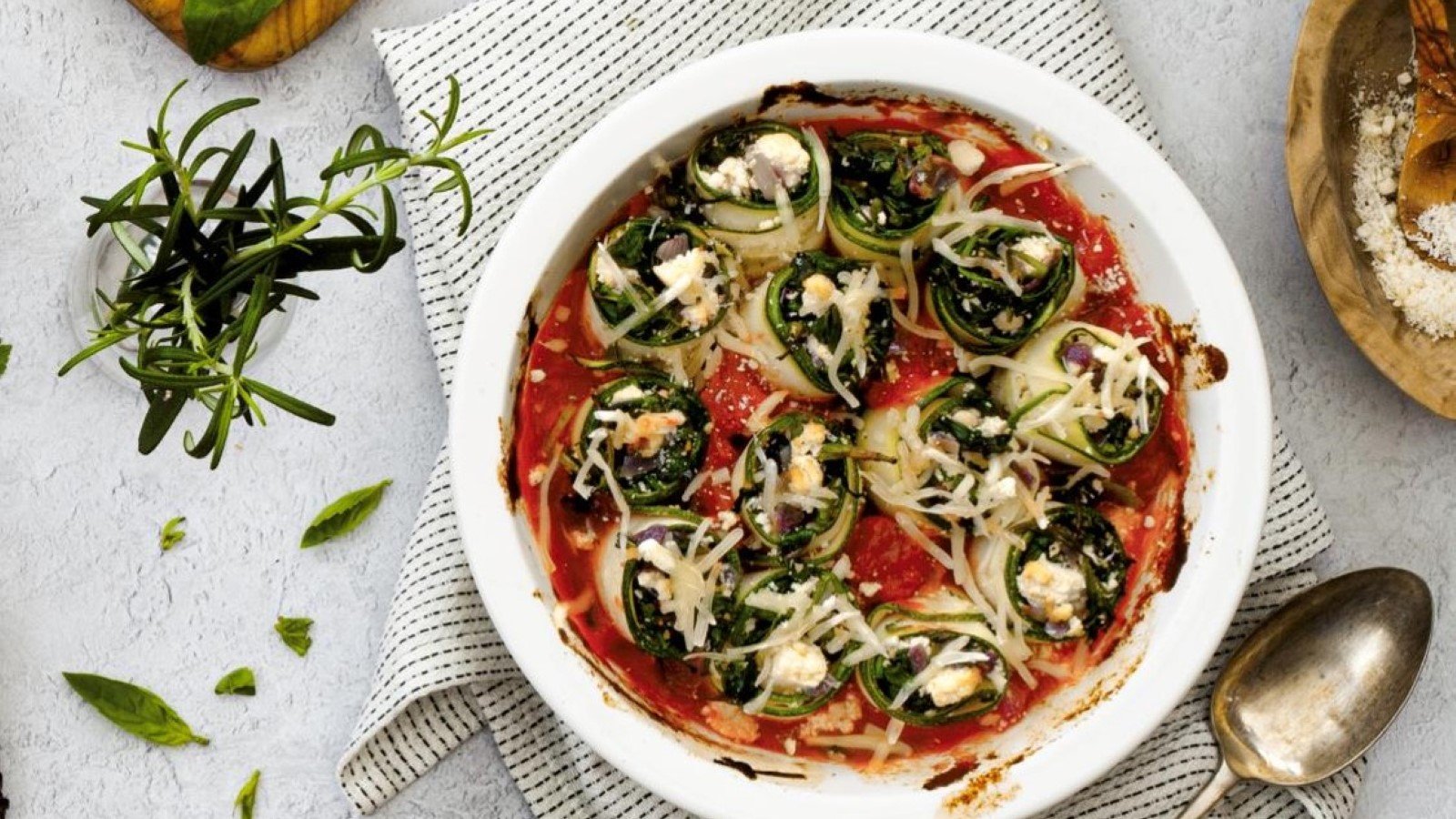 Dish of vegan tofu spinach canelloni on a table with fresh herbs and sea salt